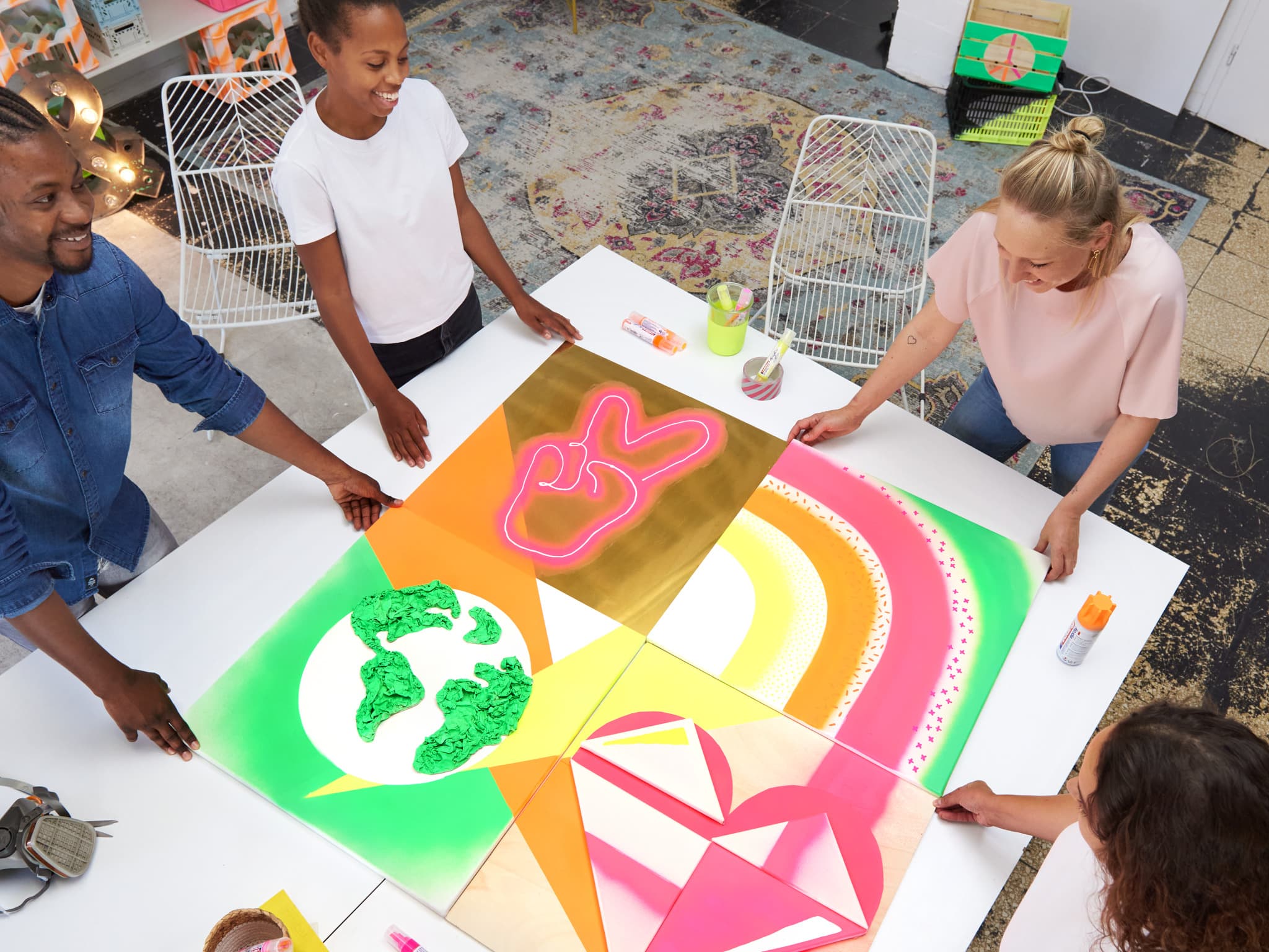 Eine Gruppe kreativer Personen arbeitet in einem hellen, künstlerischen Arbeitsbereich gemeinsam an einem farbenfrohen geometrischen Kunstprojekt mit edding 5200 Permanentspray Acryllack Neon & Kräftige Farben.