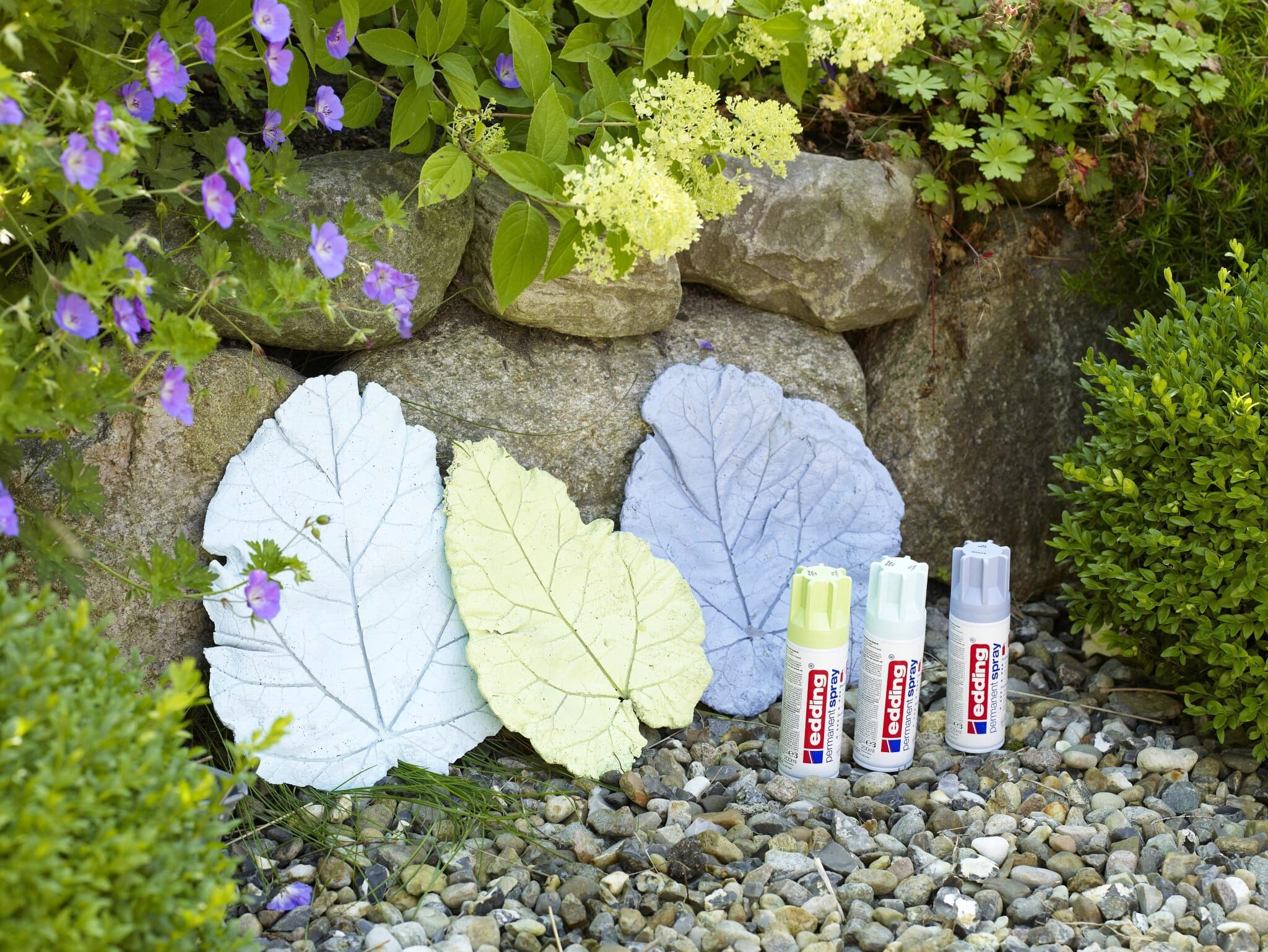 Verschiedenfarbige, blattförmige Trittsteine, die in einem Garten angeordnet sind, begleitet von edding 5200 Permanentspray Acryllack Pastell & sanfte Farben-Röhren.