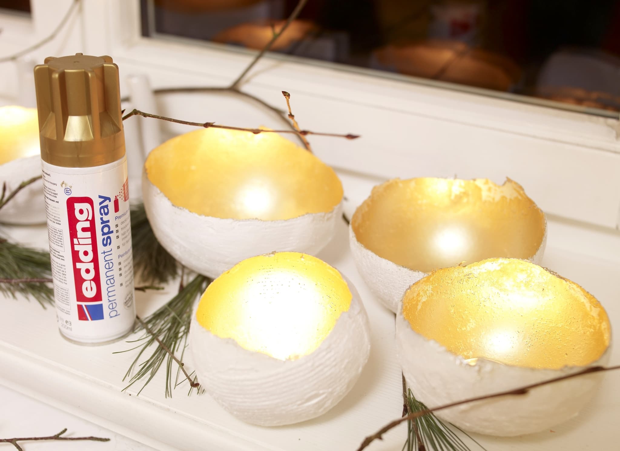 Golden bemalte Eierschalen in einer dekorativen Anordnung mit einer Dosis edding 5200 Permanentspray Metallic Acryllack in der Nähe.