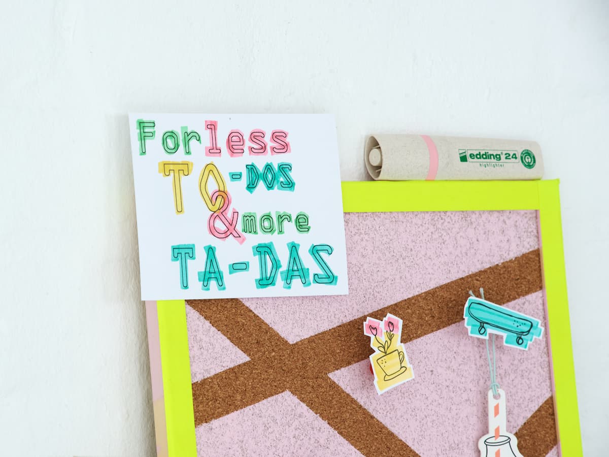 Eine farbenfrohe und motivierende Notiz an einer Pinnwand mit der Aufschrift „Für weniger To-Dos und mehr Ta-Das“ neben skurrilen Zeichnungen und einem edding 24 EcoLine Textmarker.