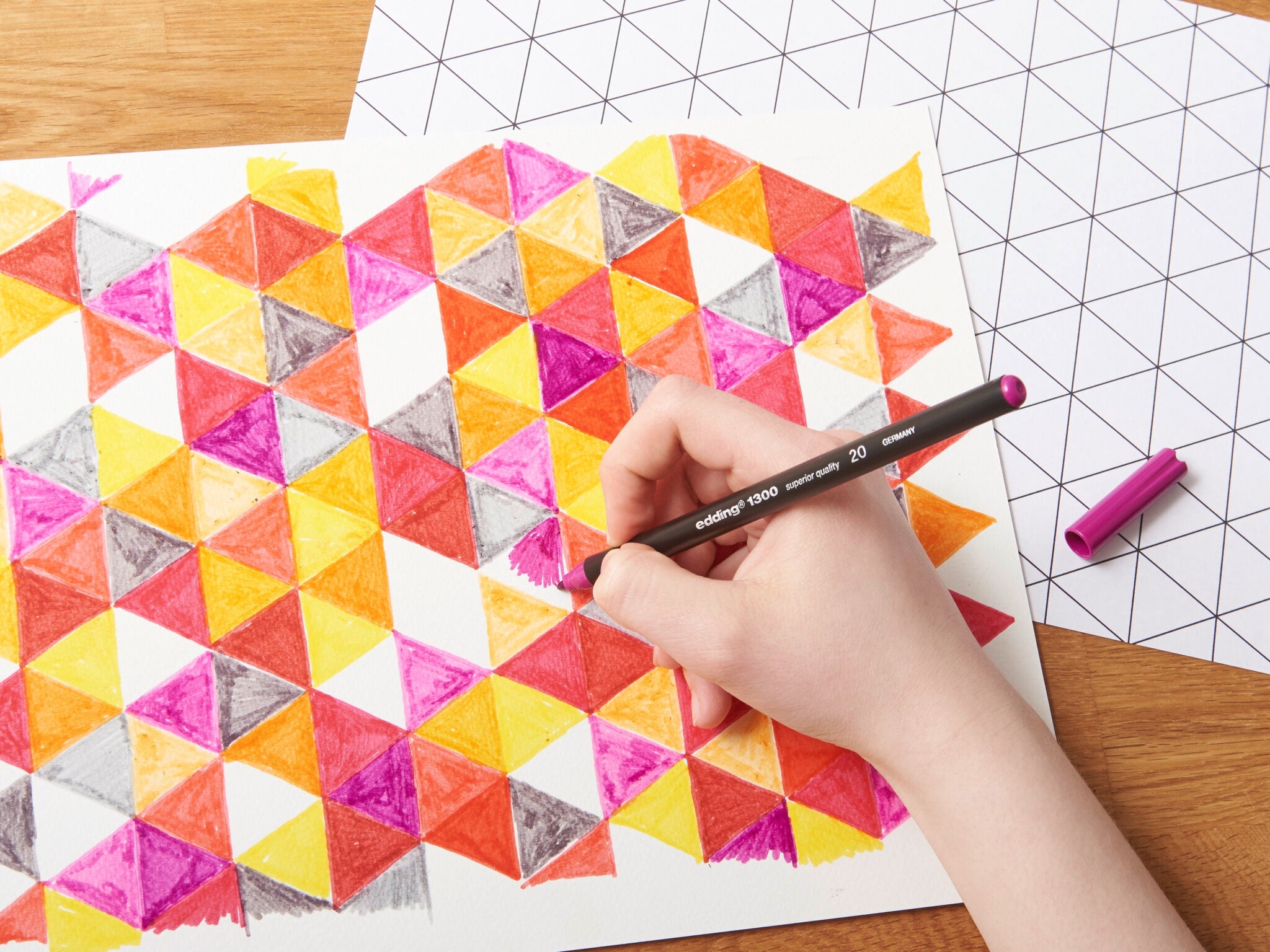 Eine Hand, die ein geometrisches Muster mit dem lebendigen edding 1300 Fasermaler-Medium auf Papier koloriert und so ein laufendes kreatives Kunstprojekt zeigt.